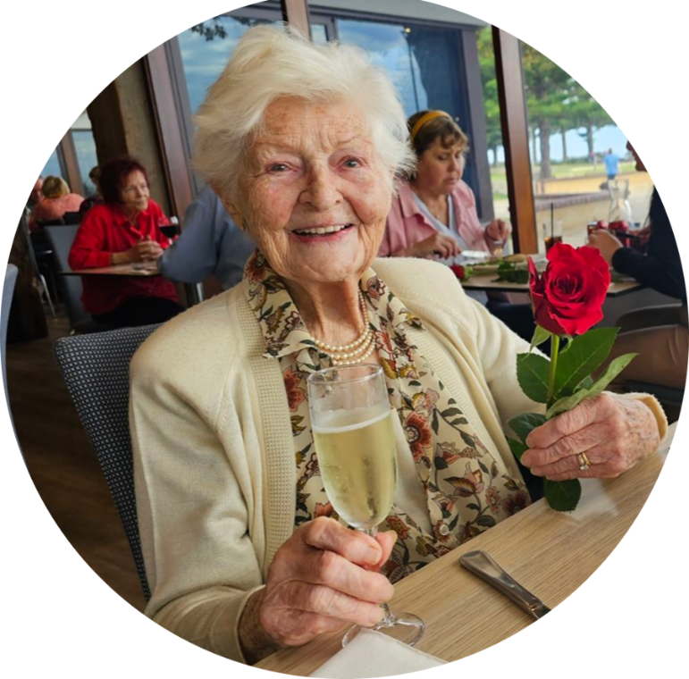 Joan Harlow smiling while holding a rose and a glass of sparkling wine